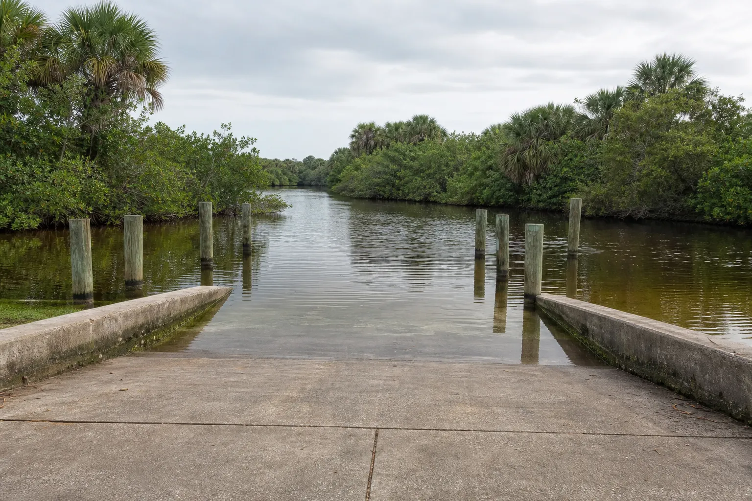 An empty concrete public boat ramp running into a tea-coloured Southwest Florida canal, lined with mangrove, under a flat overcast sky.