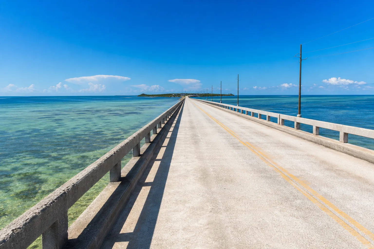 A low coastal causeway crossing shallow turquoise Gulf water under a harsh midday sun, with heat shimmer rising off the deck.