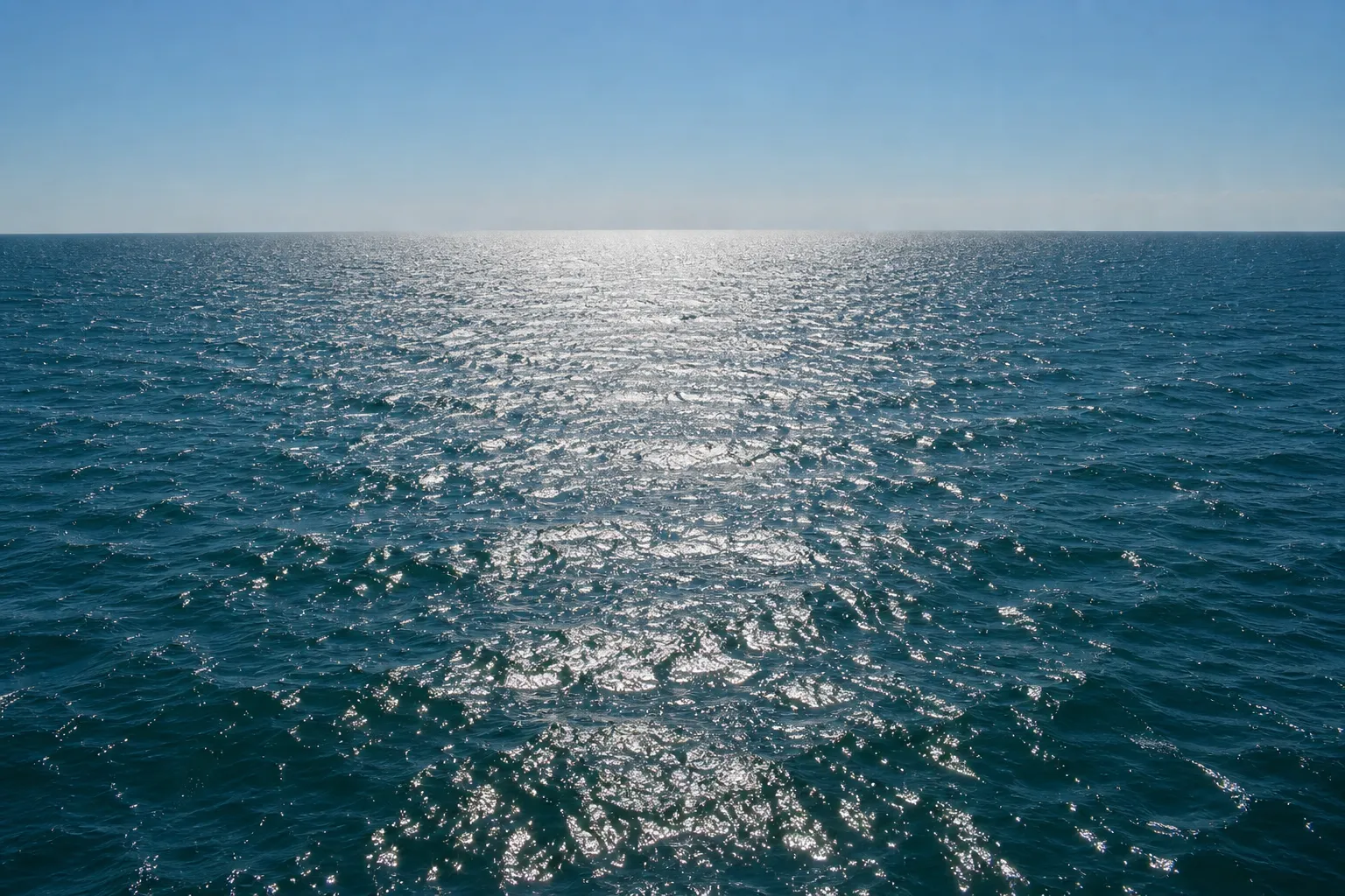 Open Gulf of Mexico swell with wind chop under a hard noon sun, deep blue-green water and a flat empty horizon.
