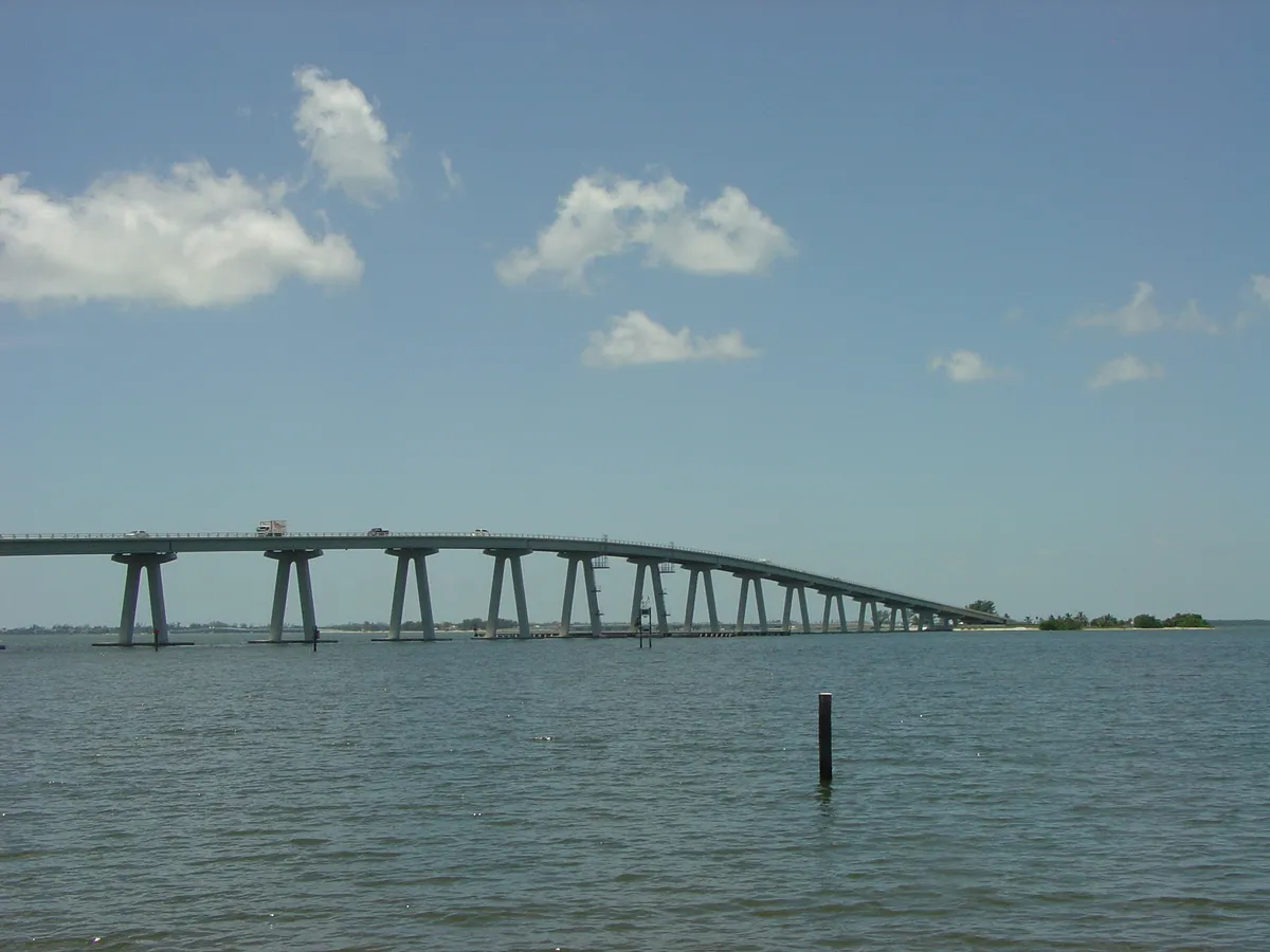 The high span of the Sanibel Causeway arcing across San Carlos Bay under scattered cumulus, seen from the water's edge.